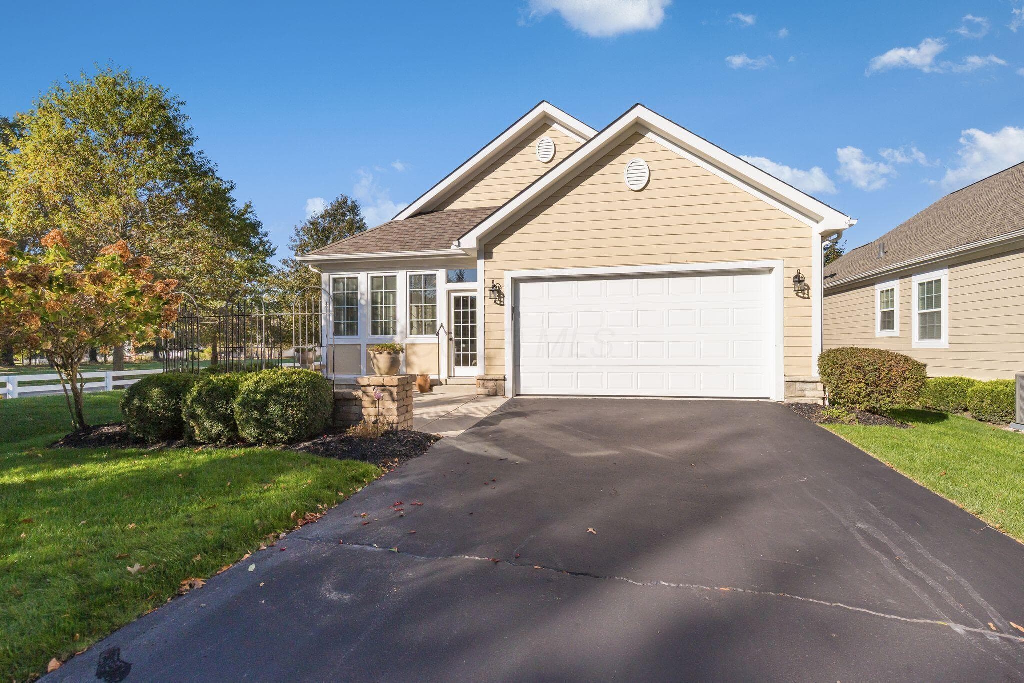 Single-story residence featuring light-toned horizontal siding, a multi-gabled roofline, an attached two-car garage, an asphalt driveway, and stone-accented exterior columns