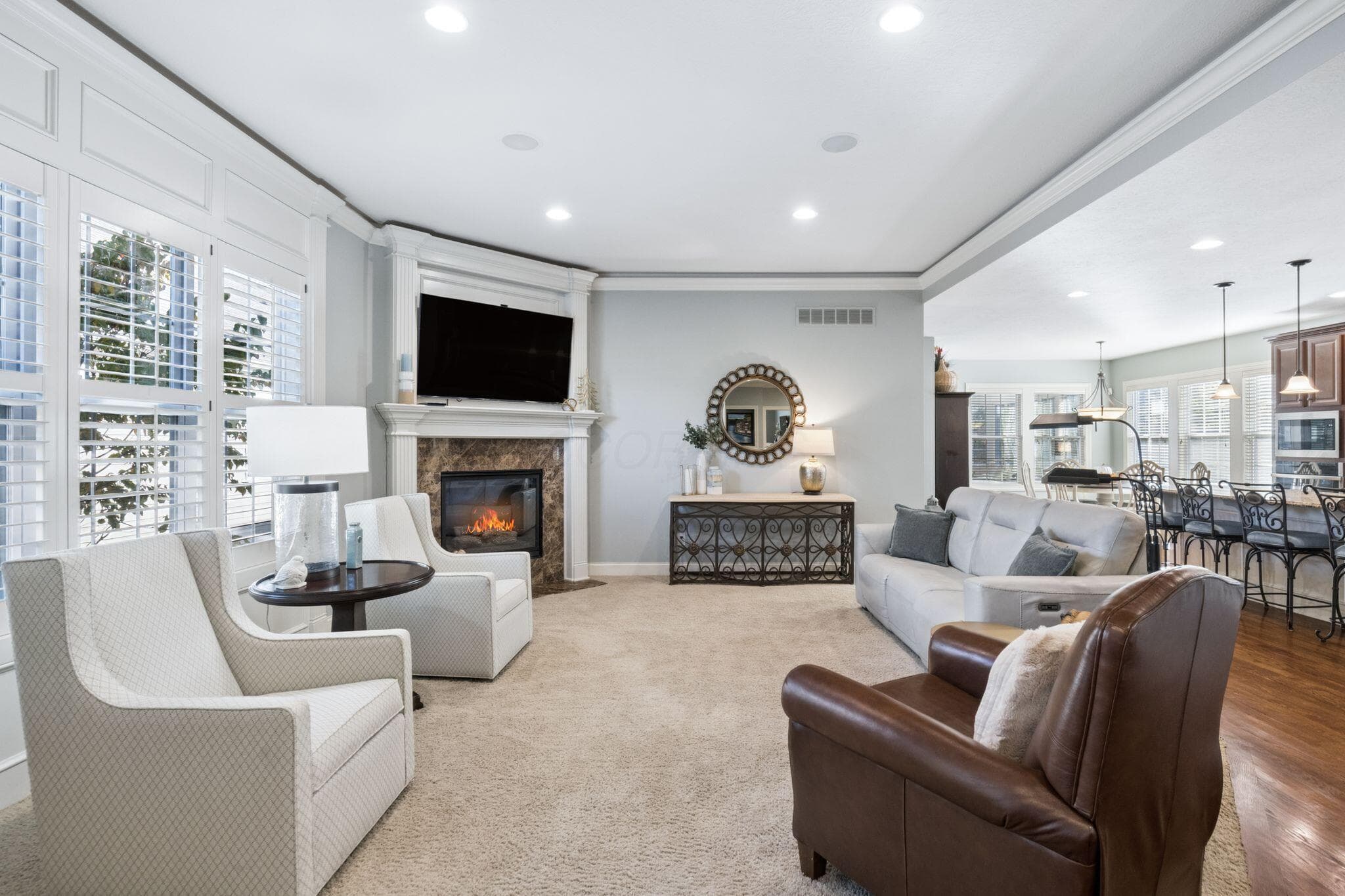 Corner fireplace with stone-surround mantel, plantation shutters, crown molding, and recessed lighting