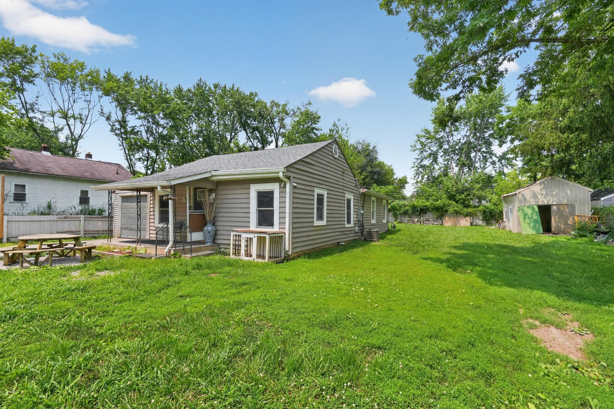 Spacious yard featuring a large green lawn, a covered patio, and a utility shed