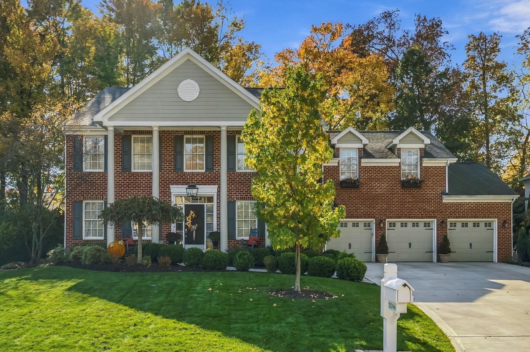 Traditional brick exterior featuring a two-story columned portico, dual dormer windows, and an attached three-car garage