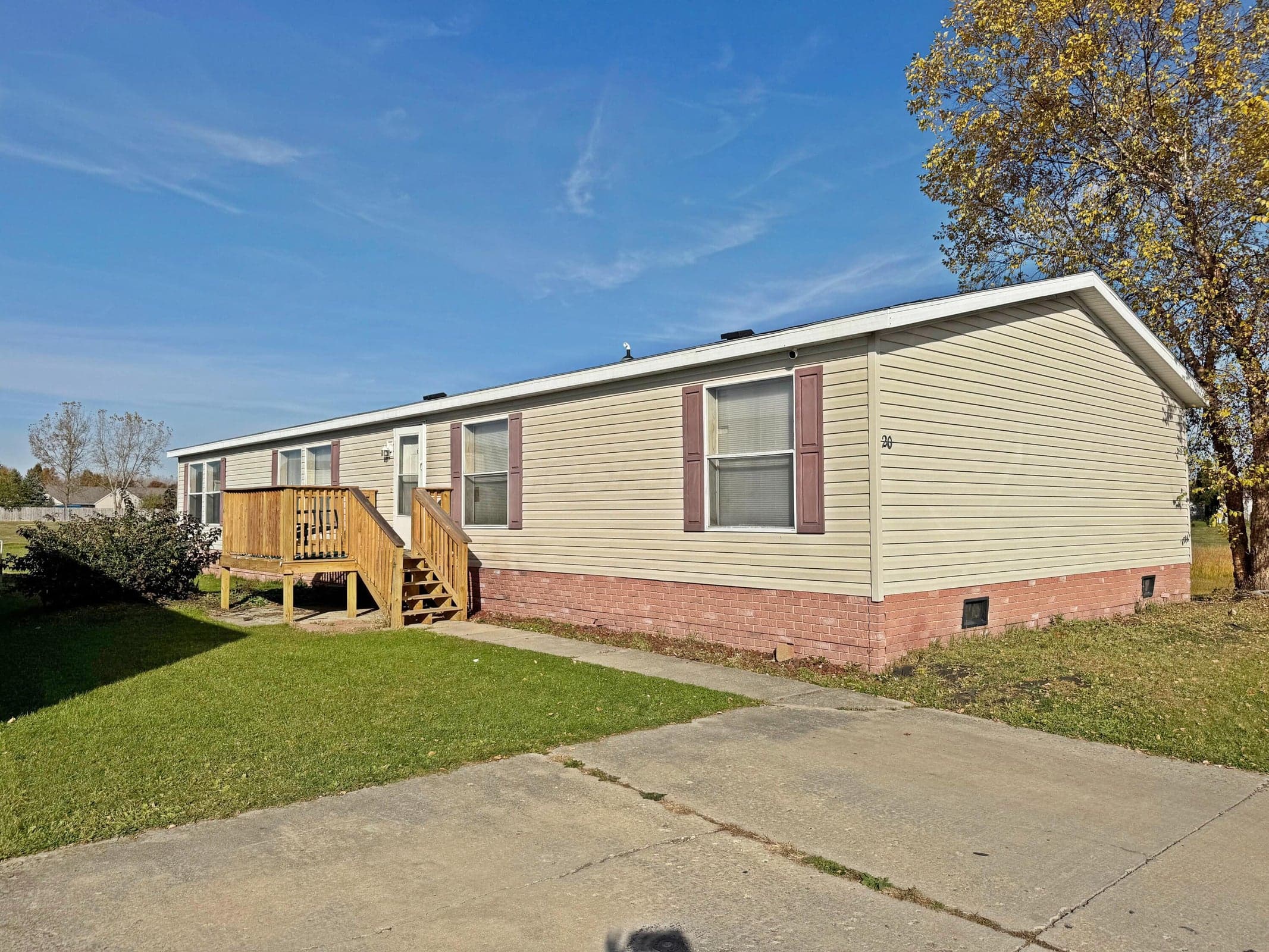 Exterior featuring beige vinyl siding, brick foundation skirting, decorative window shutters, and a wood deck