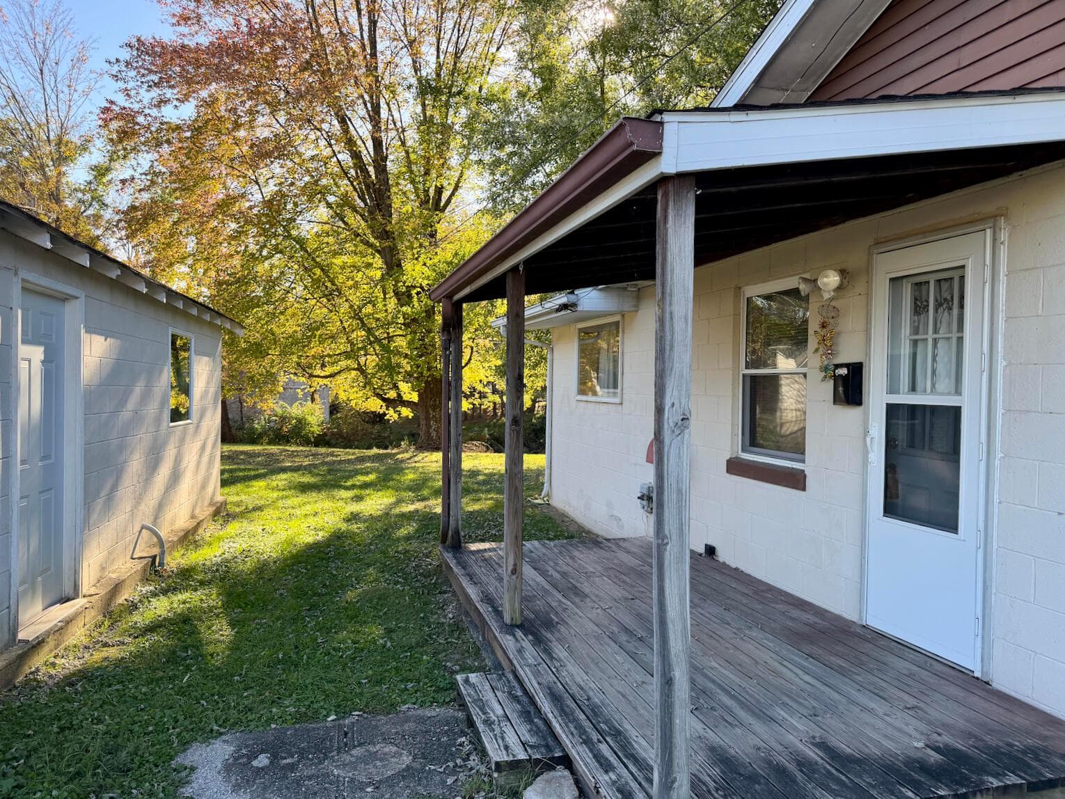Covered wooden porch, exterior masonry siding, detached structure, and expansive grounds featuring mature trees