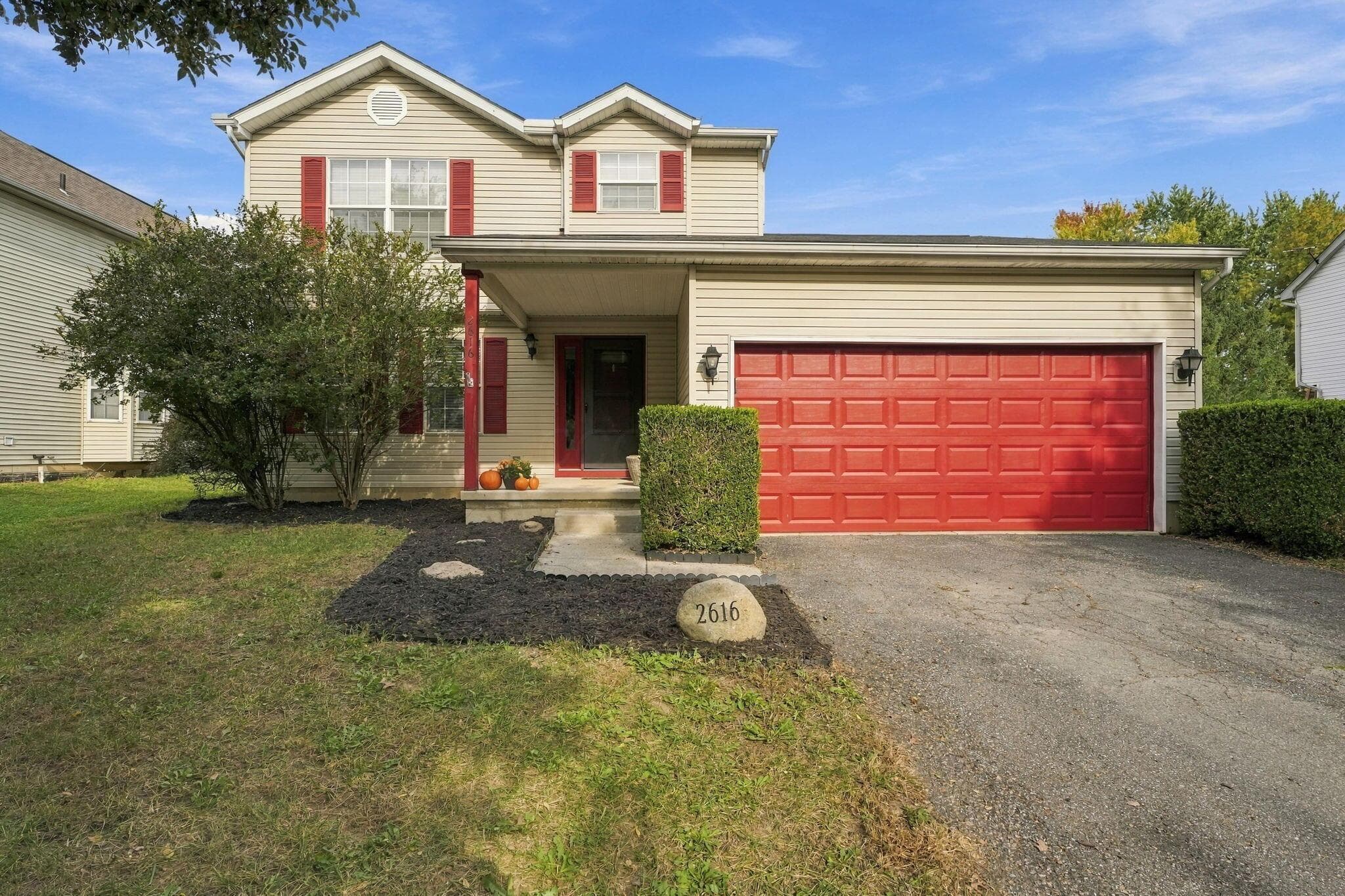 Two-story residence featuring light-toned vinyl siding, contrasting red shutters, an attached two-car garage, and an covered front entryway