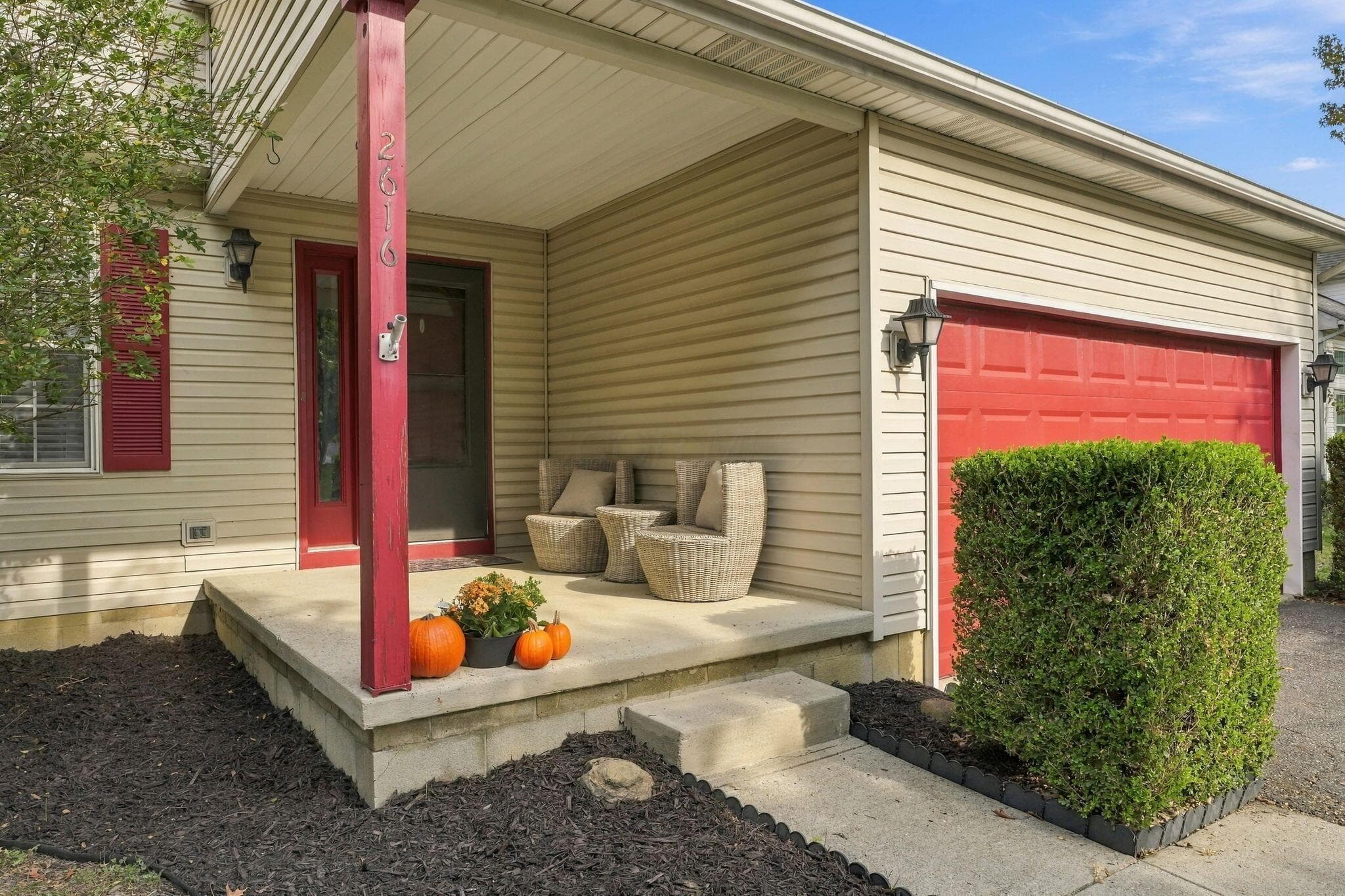 Covered front porch with a concrete stoop, vinyl siding, red garage door, and decorative exterior wall-mounted lighting