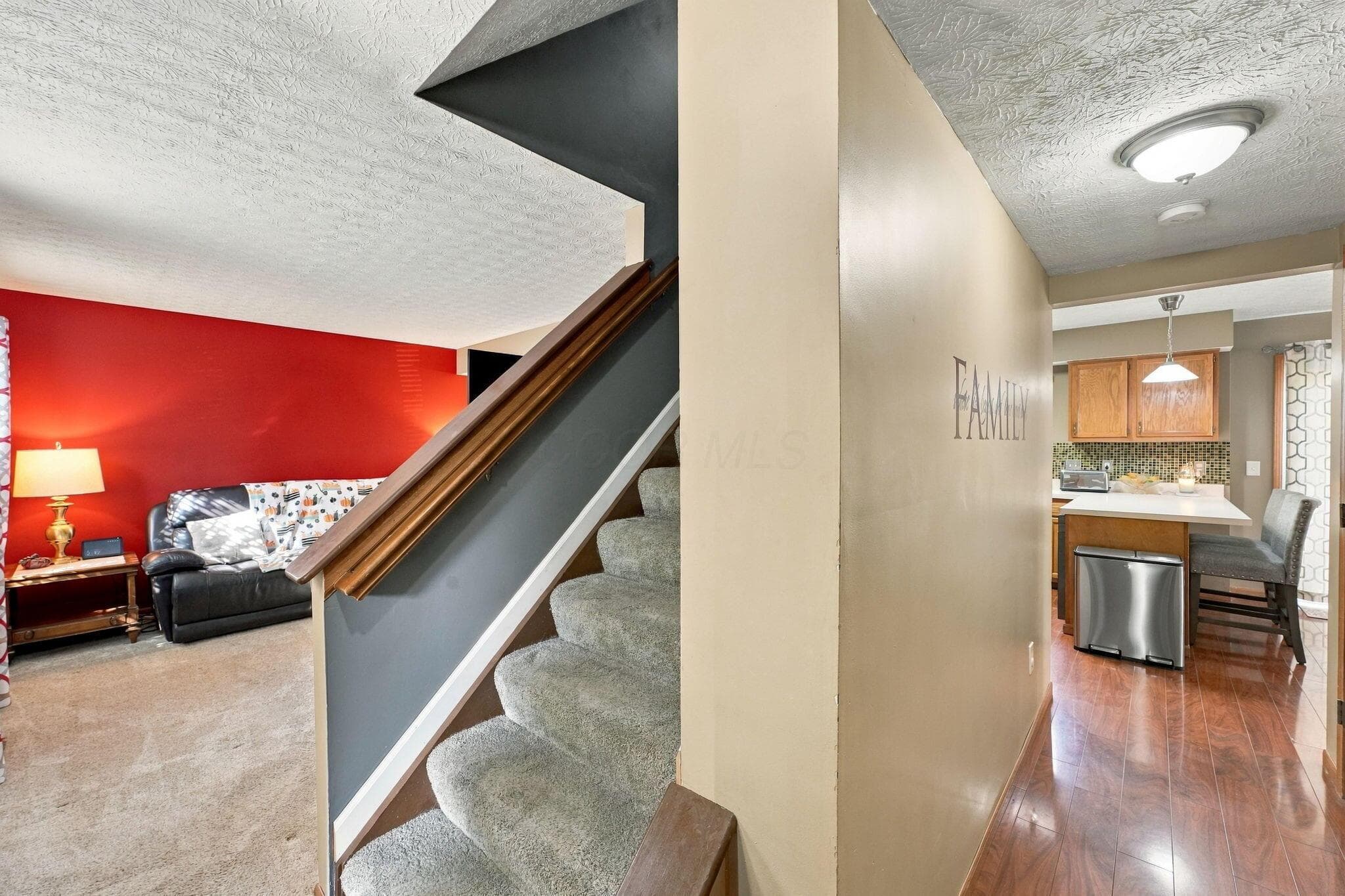 Carpeted staircase featuring a wooden handrail, wood-finish flooring, and flush-mount ceiling lighting