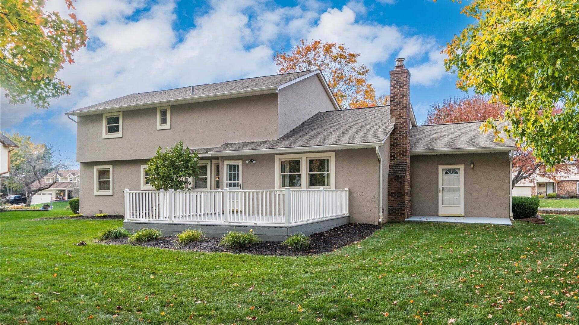 Stucco exterior featuring an elevated deck with white railing, a brick chimney, and a landscaped lawn