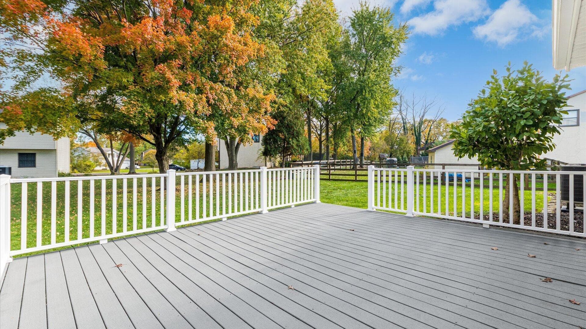 Composite decking with white vinyl perimeter railing, overlooking a level lawn enclosed by split-rail fencing and mature trees