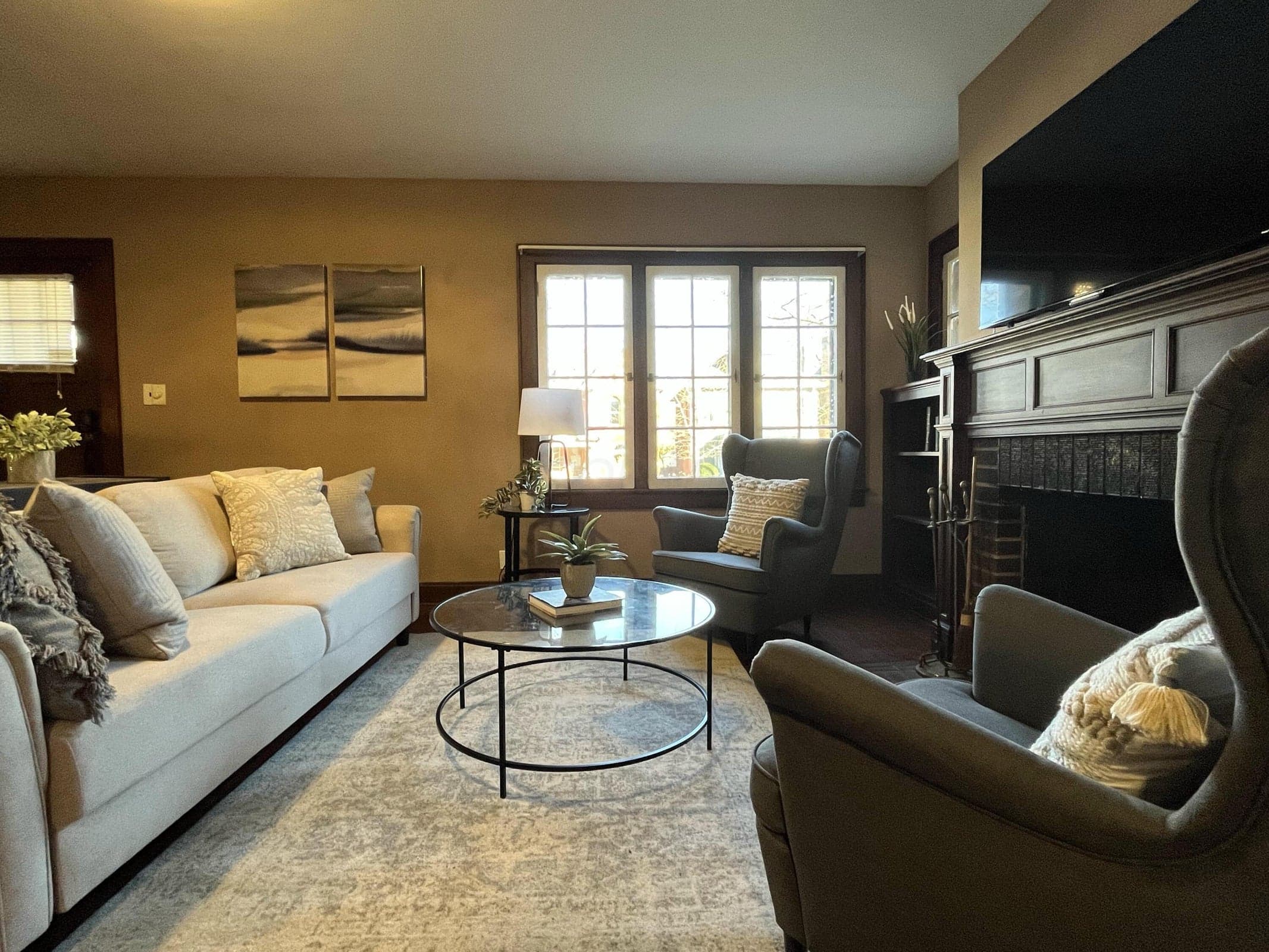 Three-panel window, fireplace with dark wood mantel, built-in shelving, and wood-finish flooring