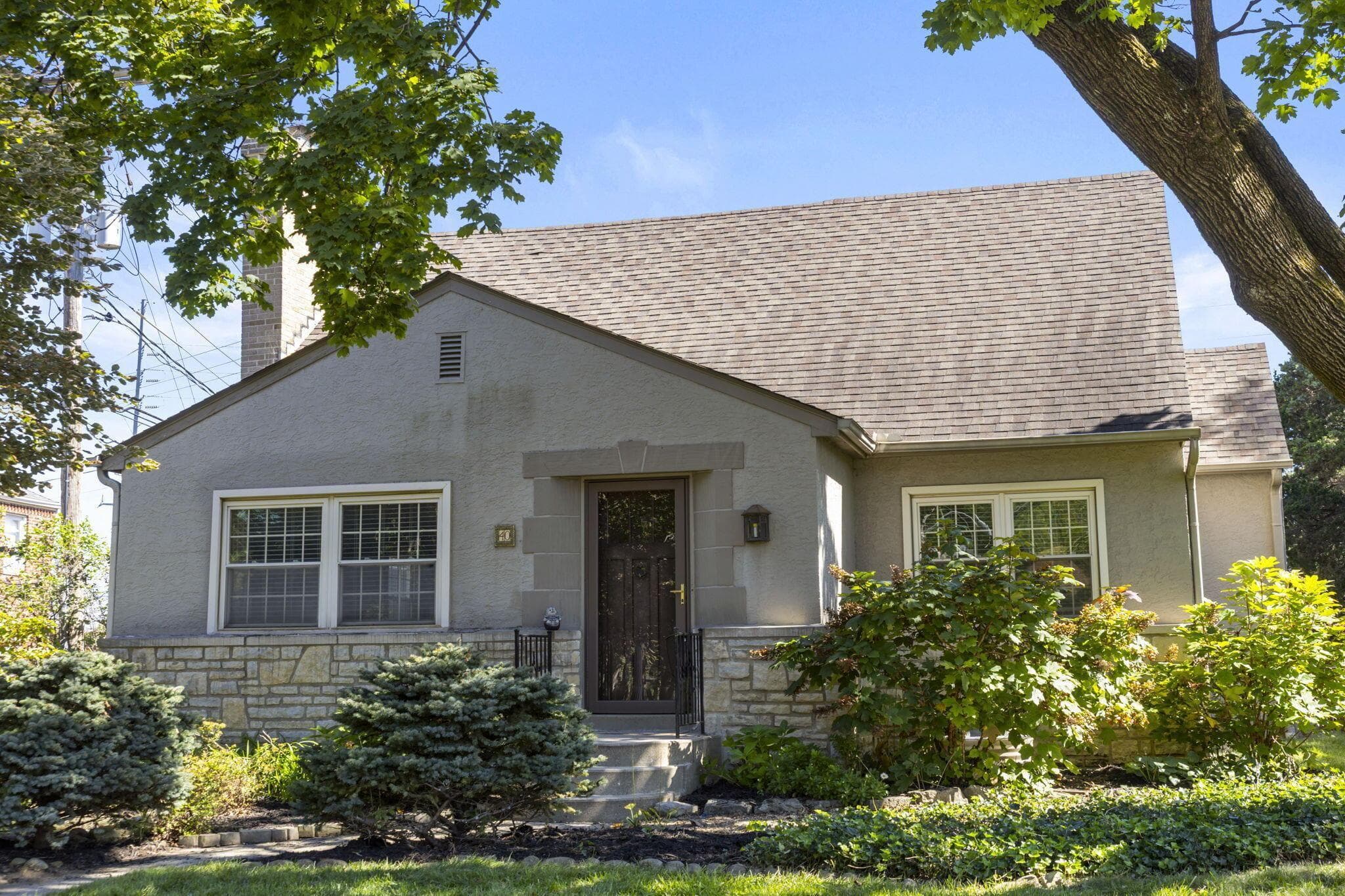 Stucco exterior with stone accent siding, gabled roofline, front entry door with storm door, and mature landscaping